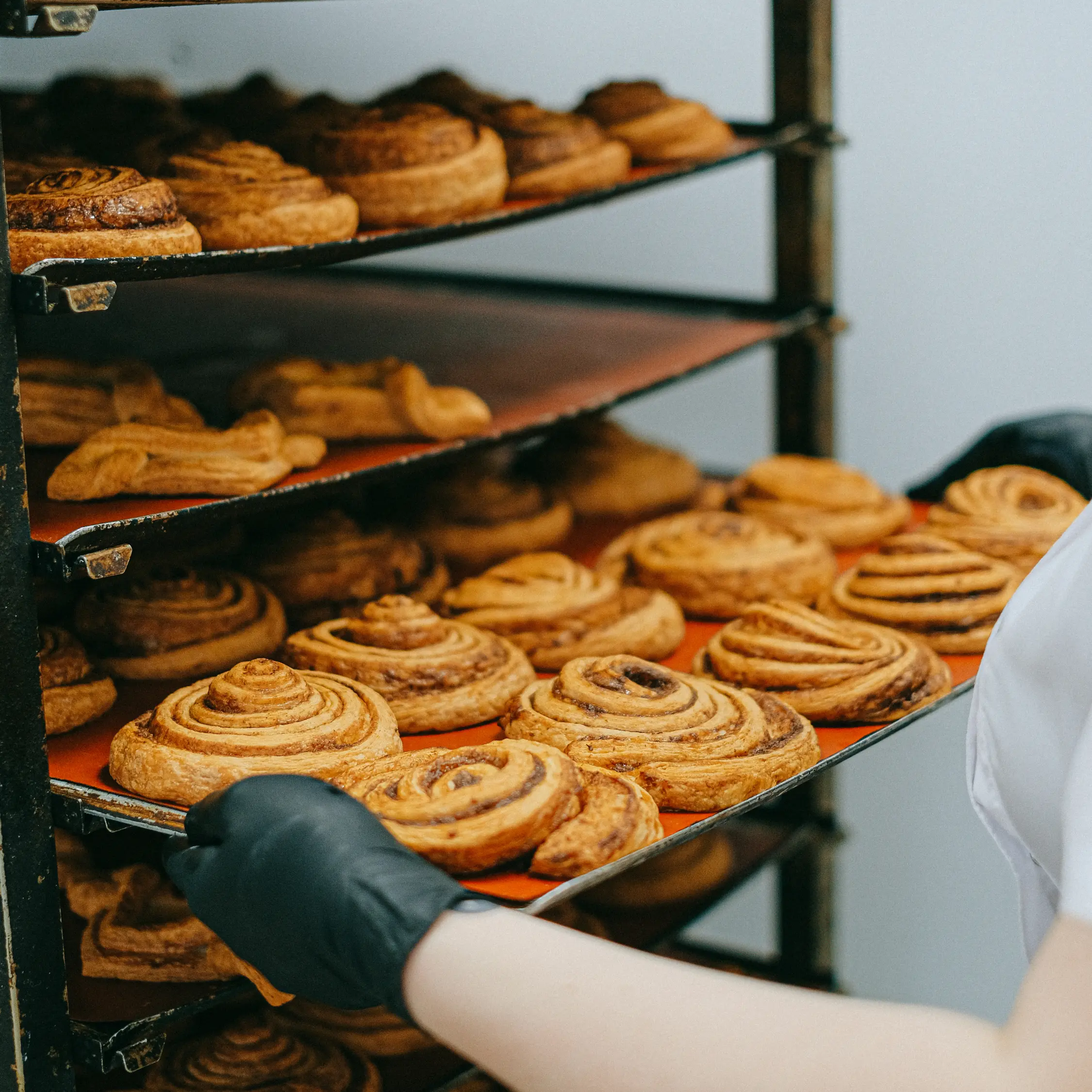 Baker loading trays of fresh cinnamon rolls into bakery rack oven at Vonado Cookie and Bread in Hanoi